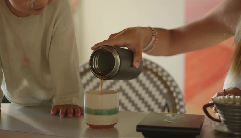 Mother with a small child by her side pouring coffee into a cup