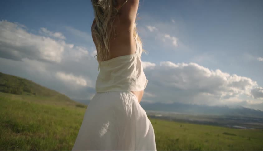 A pregnant blonde woman stretches while standing on a grassy field