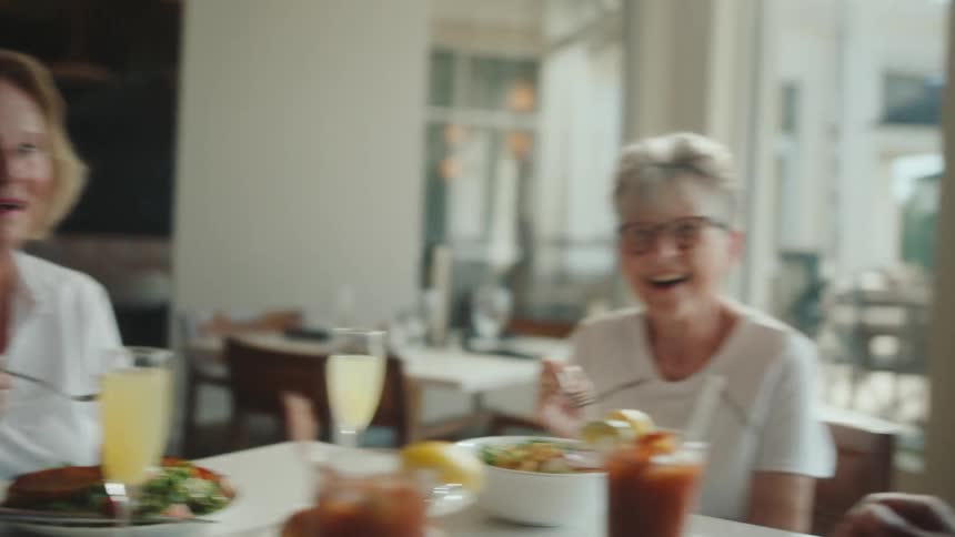 Four people in a restaurant talking and smiling over food and drinks
