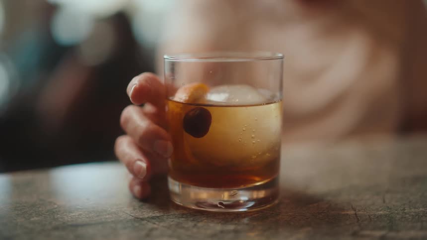 Woman rotating an old fashion drink while sitting at a bar