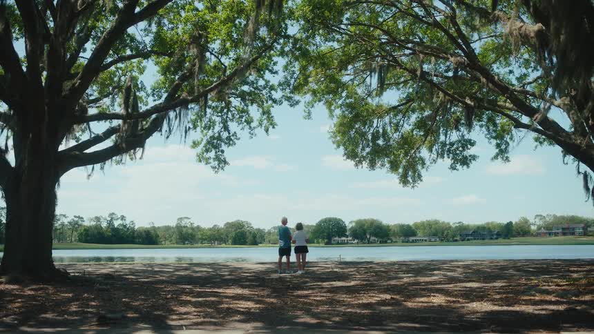 Man and woman in the background by a lake in a garden talking
