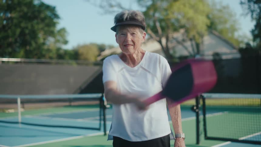 Elderly lady swings a pickleball paddle on a tennis court