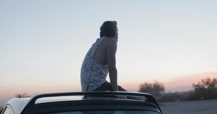 Man sitting on the rooftop of his vehicle and looking at a clear sunset