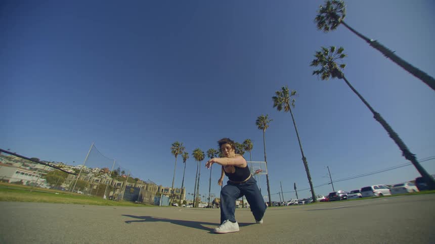 A woman is doing dance moves on a concrete floor on a clear blue sky day
