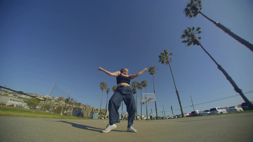 A woman is making dance gestures on a concrete floor with some trees to the right