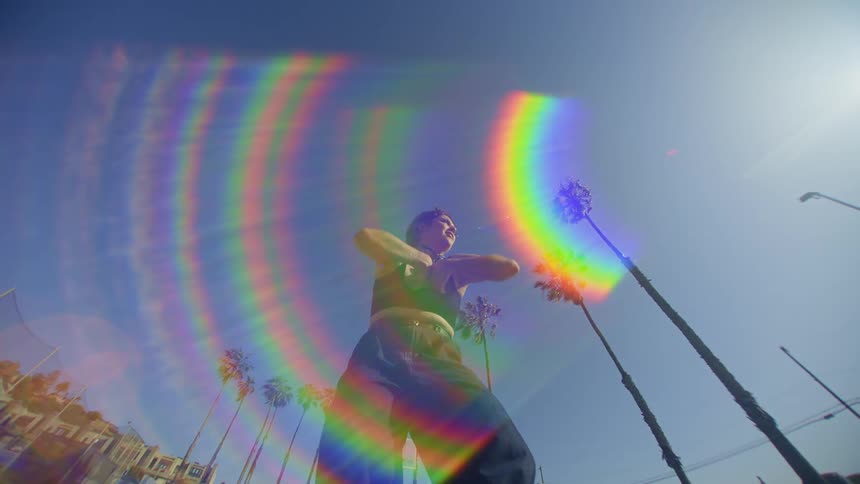 The sun streaks a rainbow over the dancing woman