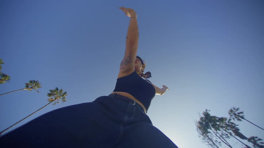 Upward view of a woman dancing against a blue sky in an outdoor setting