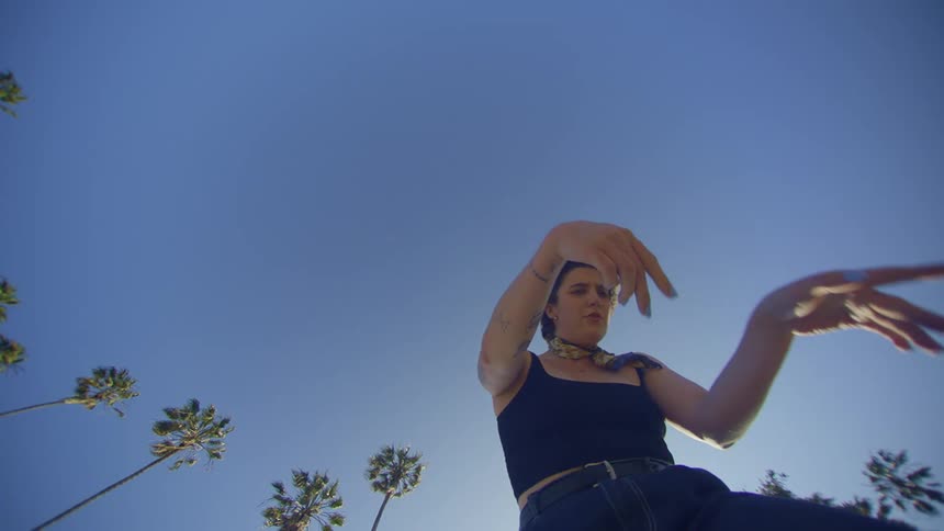A young woman is making movements with her arms and hands in contrast to the blue sky