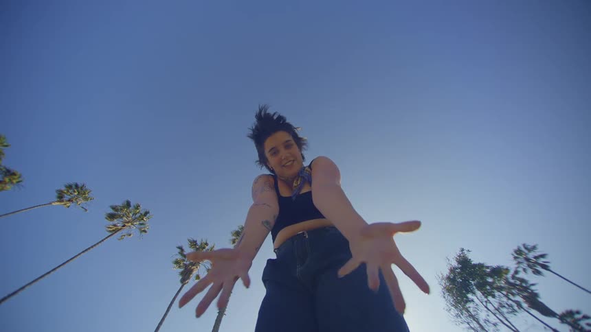 A white woman smiles while dancing near palm trees