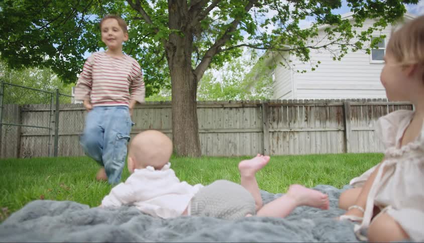 Two children lying on a blanket in the grass and in the background a child running
