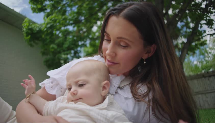 A mother kisses her baby while they lie on a lawn