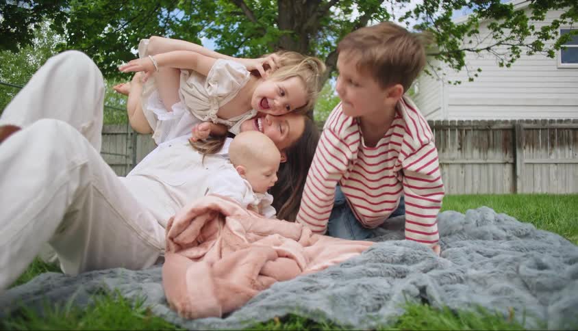Three little children around their mother in a grassy garden in the backyard
