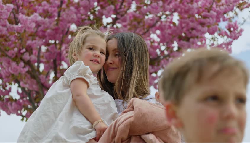 Mother hugging a baby and a little girl and another son in front of her while they are under a pink tree