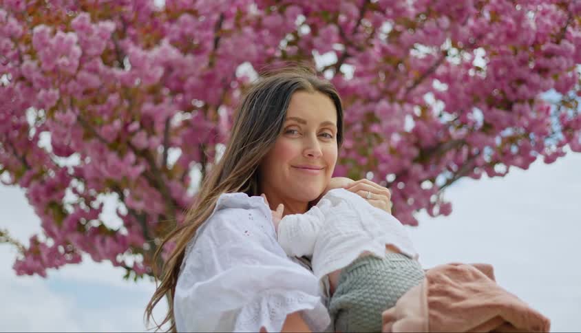 A mother holds her baby near a tree in full bloom