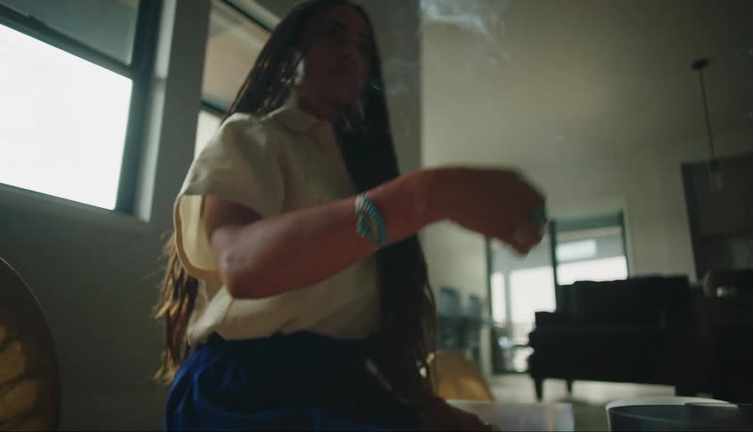 A woman is shaking an object that is burning to release smoke and she places it in front of her