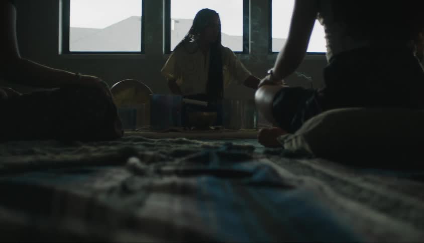 Some people are sitting and one of them has an object in his hand that is releasing smoke