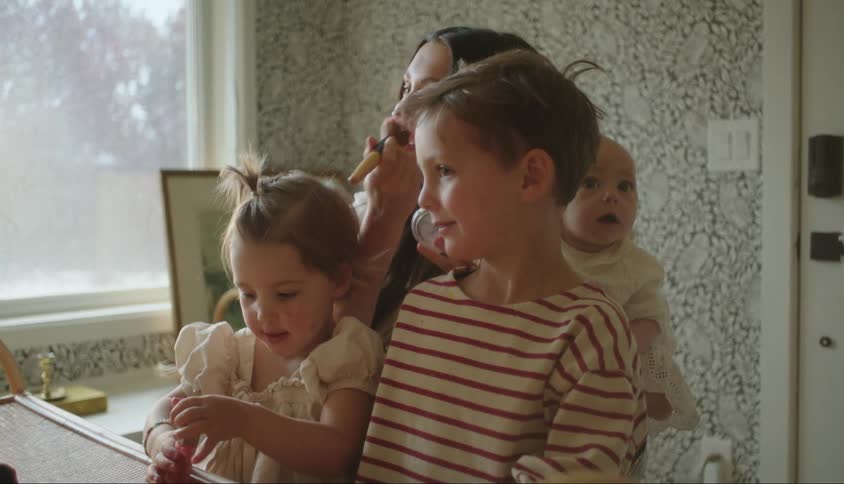 A mother applies makeup while surrounded by her children