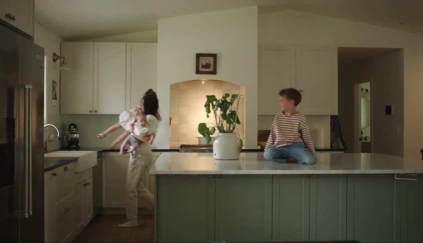 Mother carrying a baby and a little girl on her lap and placing another boy next to the sink on a counter in the kitchen