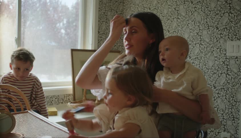 Mother holding baby putting make up on as her other kids surround her