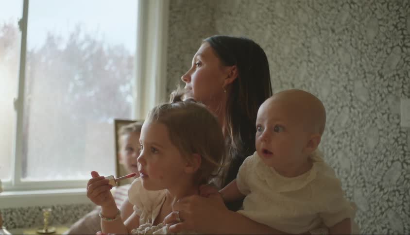 A mother sitting at a table with her children applying makeup at home