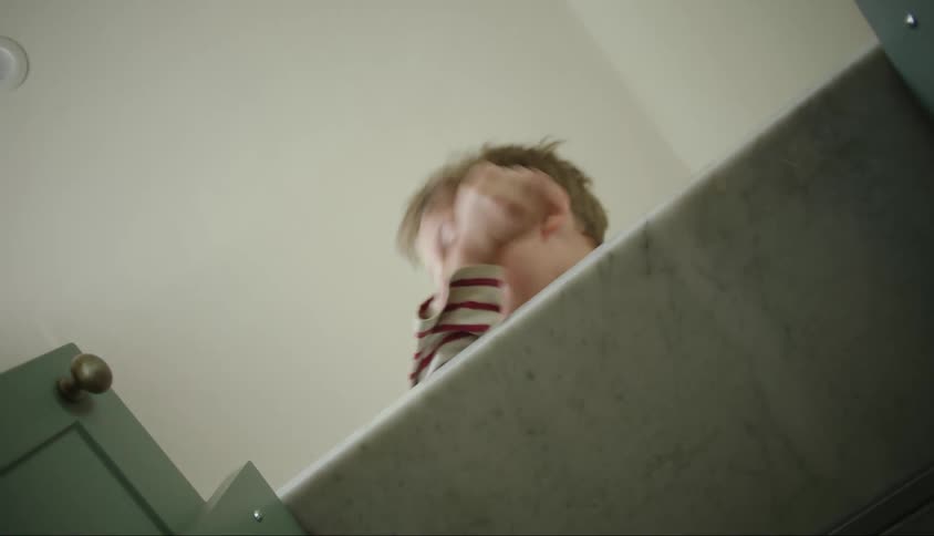 A little boy is on top of a piece of furniture and starts talking and leaves