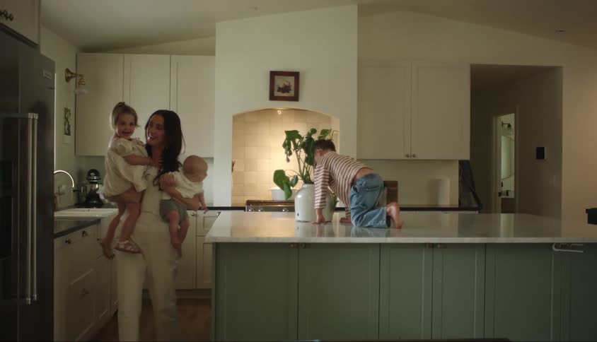 Mother picking up a child and holding a baby on her lap and her other small child on a counter