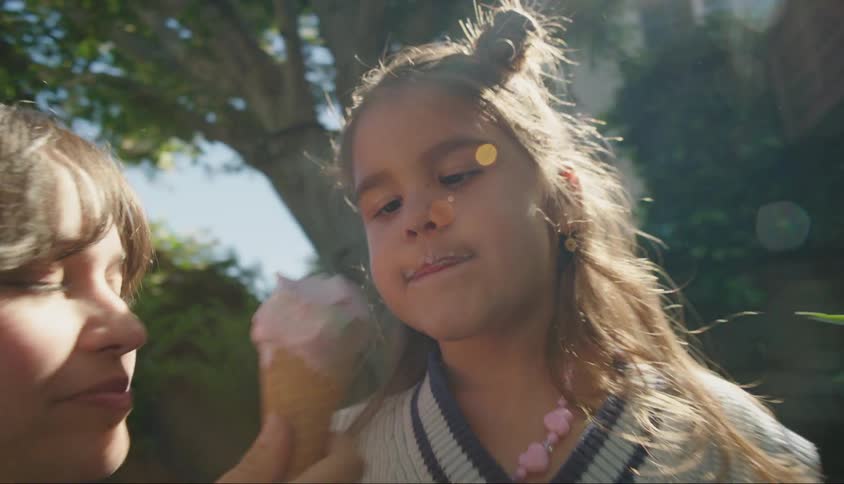 A mother and daughter share an ice cream cone in a garden