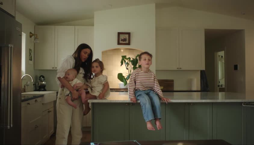 A mother plays with two of her children as her son sits nearby
