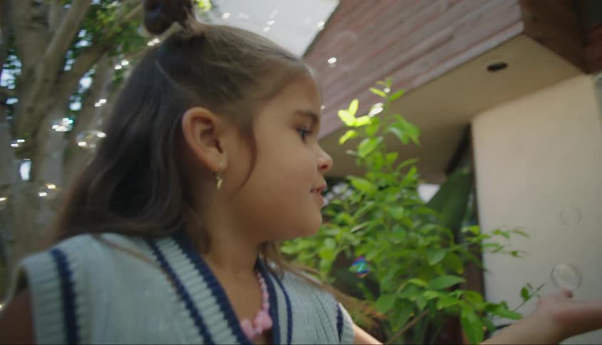 Little girl in the backyard with one of her hands open and soap bubbles falling