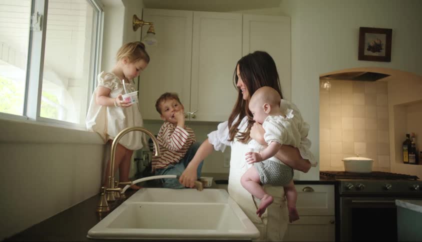 A woman is using the sink as her children walk on the counters