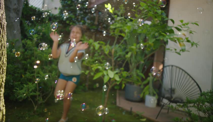 Girl playing in the backyard with soap bubbles that are flying