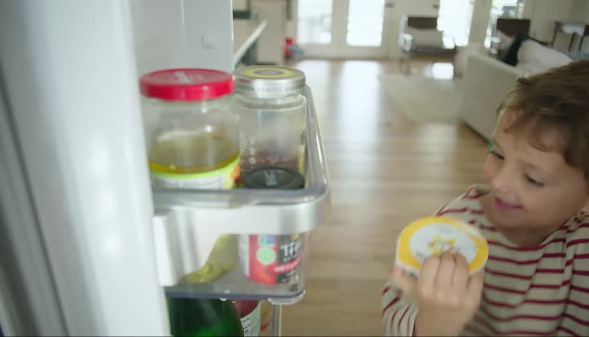 A young boy takes a container of yogurt out of a refrigerator and dances for joy