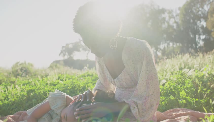 A mother caresses her young daughter as they sit and lie in a field