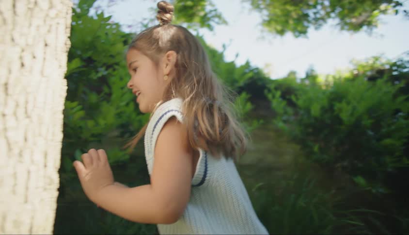 Smiling little girl running around a log in a yard