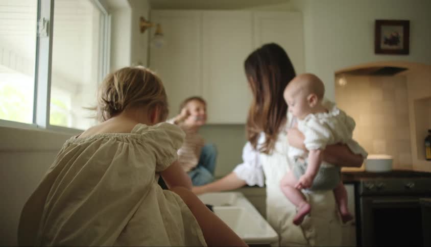Mother in the kitchen holding a baby on her lap and two other children around her eating