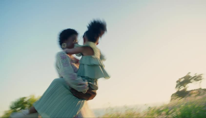 A mother spins her daughter around while they are standing in a field by a coast