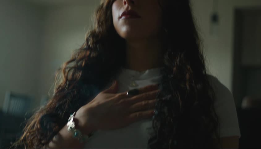 Portrait of a young curlyhaired woman indoors placing her hand on her chest