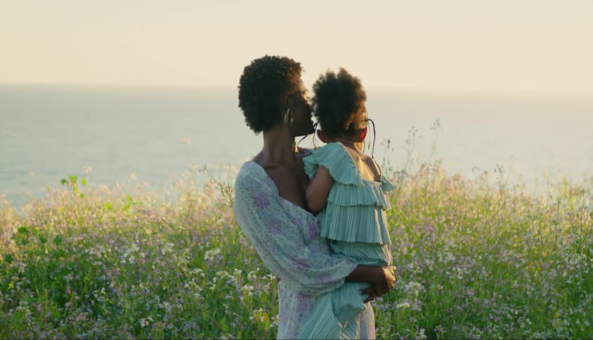 Mother holding her little daughter on her lap while they are in a field with flowers