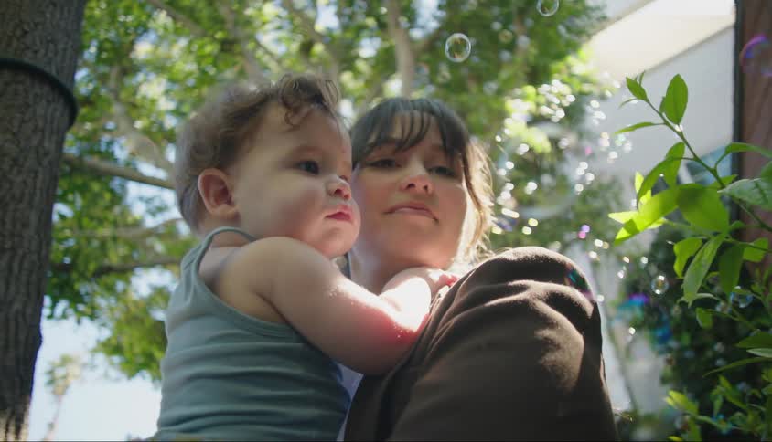 A woman holding her baby on her lap and there are several soap bubbles around