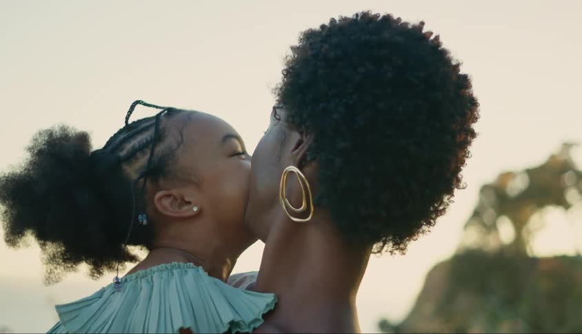 A woman has her daughter on her lap and they are both smiling and the woman is trying to kiss her on the cheek