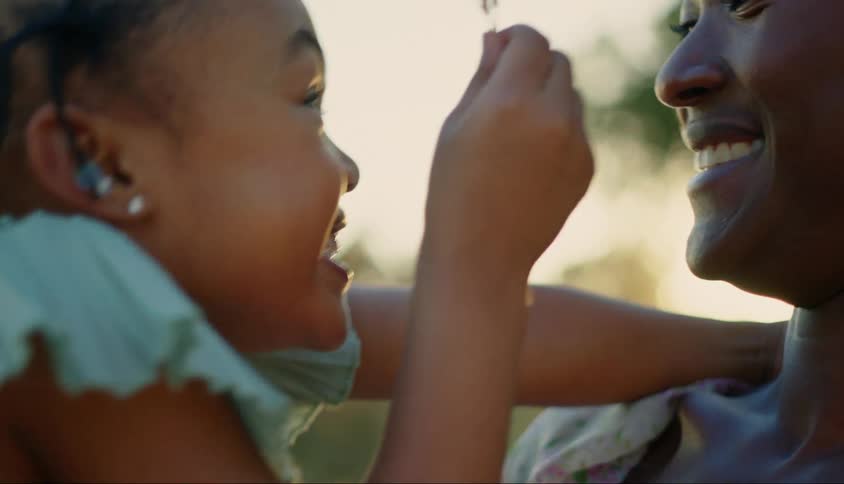 A young girl holds a flower and laughs with her mother