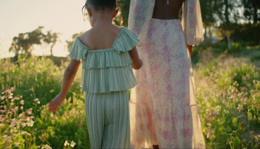 A child holds her mothers hand as the walk through a field together at sunset