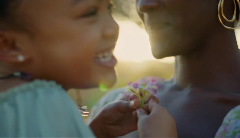 Smiling mother holding her daughter on her lap who is holding a small flower in her hands