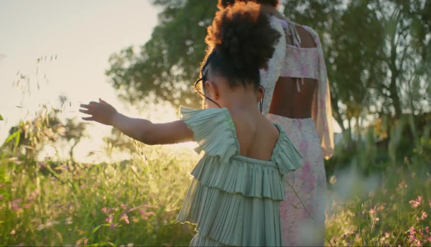 Mother walking hand in hand with her little daughter in a garden with flowers and the suns reflection on the horizon