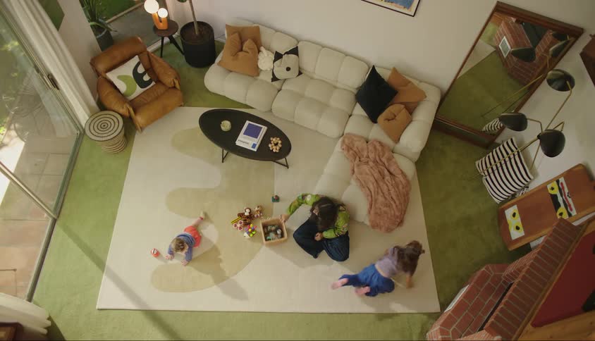 A mother sits on a living room floor as her two children crawl around
