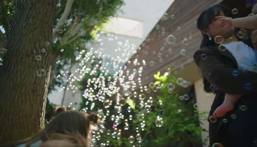 A mother and her two children surrounded by floating bubbles outdoors