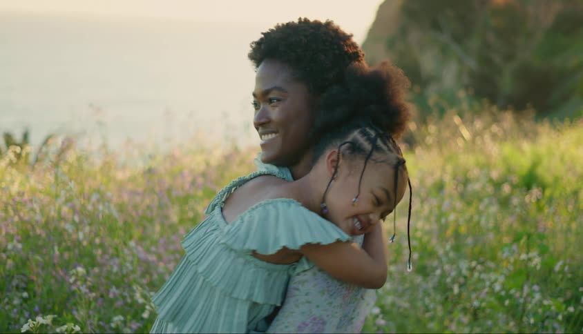 Mother with her daughter on her lap hugging each other while they are in a garden in a natural environment