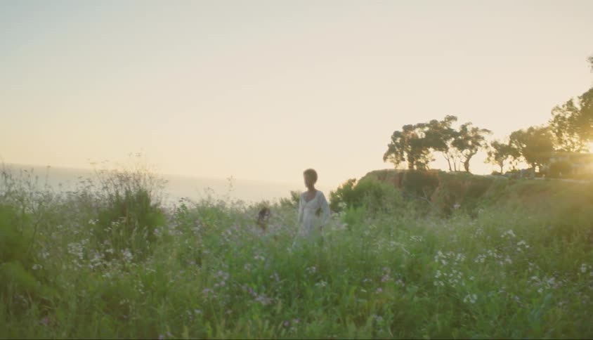 Woman and daughter run through a coastal field of wildflowers at sunset