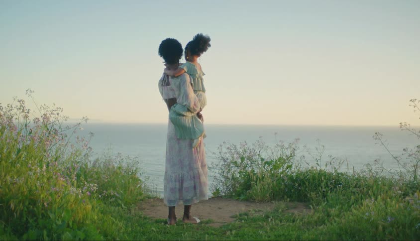 Mother holding her daughter on her lap while they are on a vegetationcovered beachfront in the late afternoon