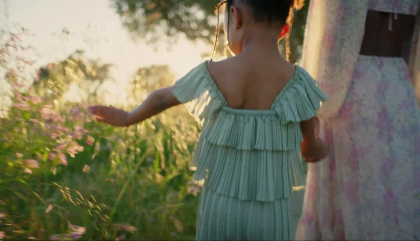 Daughter touches flowers while walking along path hand in hand with her mother